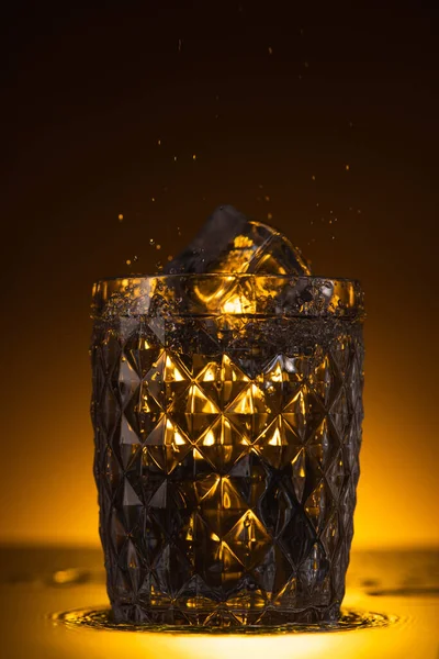 Vidro Facetado Com Cubo Gelo Vodka Espirrando Escuro Com Luz — Fotografia de Stock