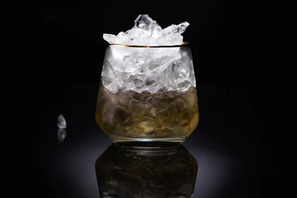 透明玻璃杯 有冰块和黑色底色的金色液体 — 图库照片