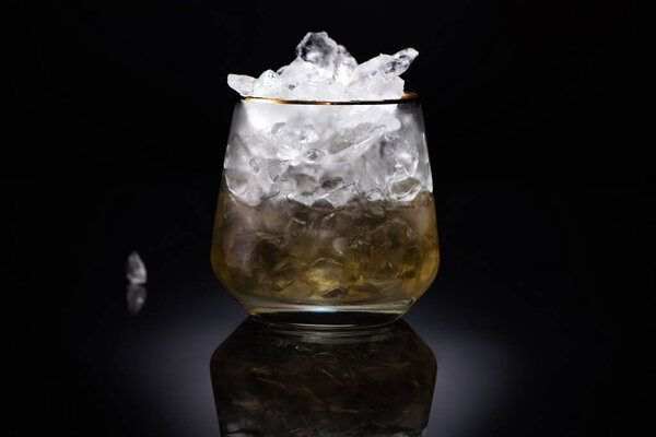 transparent glass with ice and golden liquid on black background