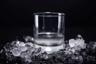 transparent glass with vodka near smashed ice on black background clipart