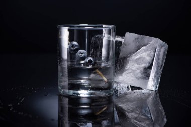 transparent glass with vodka and blueberries near ice cubes on black background clipart