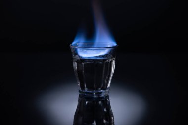 transparent glass with burning liquid on black background clipart