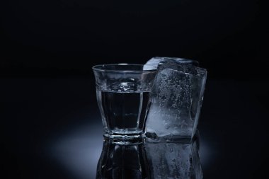 transparent glass with ice cube and vodka on black background clipart