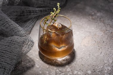 transparent glass with herb, ice cube and whiskey on concrete surface with mesh cloth clipart