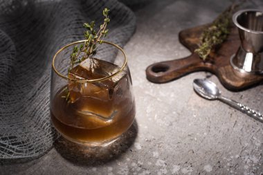 selective focus of transparent glass with herb, ice cube and whiskey on concrete surface with bar equipment clipart