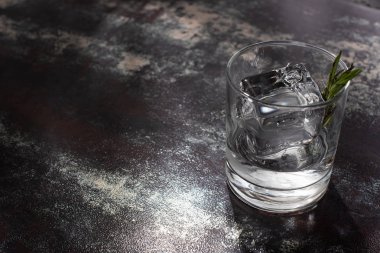 biberiyeli şeffaf cam, buz küpü ve yıpranmış yüzeyde votka.