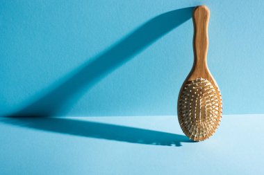 Wooden hair brush with shadow on blue background, zero waste concept clipart