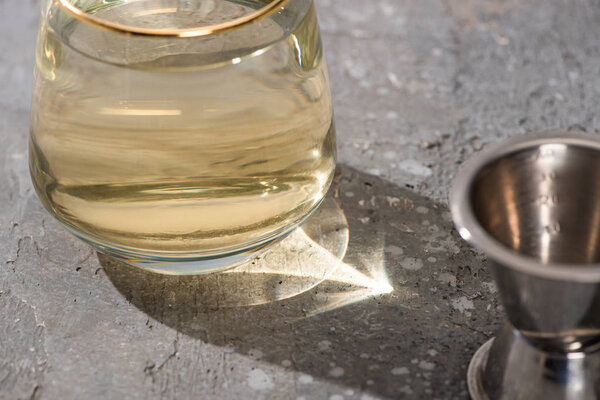 selective focus of transparent glass with golden liquid on concrete surface with jigger