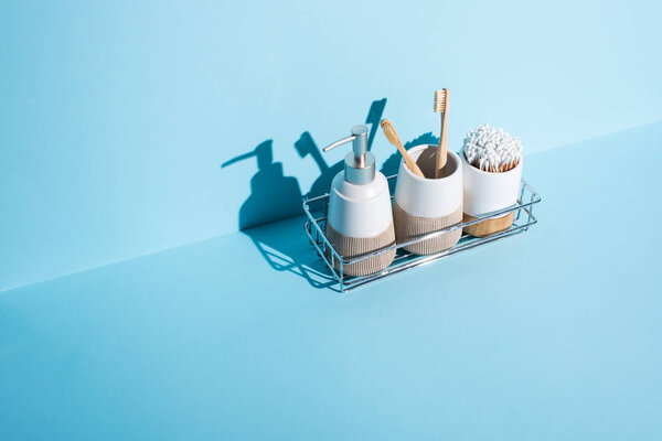 Toothbrush holders with ear sticks and toothbrushes with dispenser liquid soap on bathroom shelf on blue background, zero waste concept