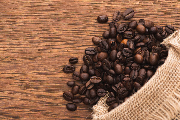 top view of fresh roasted coffee beans scattered from sack on wooden surface