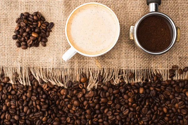 Ovanifrån Färska Rostade Kaffebönor Och Säckväv Med Cappuccino Och Filterhållare — Stockfoto