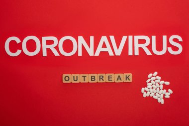 Coronavirus harflerinin üst görüntüsü ve kırmızı arka plandaki hapların yanındaki tahta küplerde salgın.