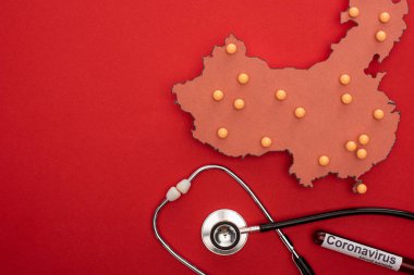 Çin haritasında steteskoplu raptiyelerin üst görüntüsü ve kırmızı arkaplanda koronavirüs harfli test tüpü.