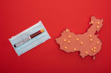 Çin haritasının üst görünümü Coronavirus harfleriyle test tüpü ve kırmızı arka planda tıbbi maske.