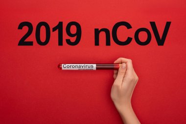 Üzerinde kan örneği olan test tüpü tutan kadının üst görüntüsü ve kırmızı yüzeyde 2019 ncov harfleri, panoramik çekim.