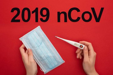 Top view of woman holding medical mask with thermometer near 2019 ncov lettering on red surface clipart