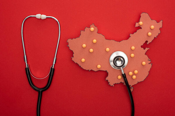 Top view of map of china with push pins and stethoscope on red background 