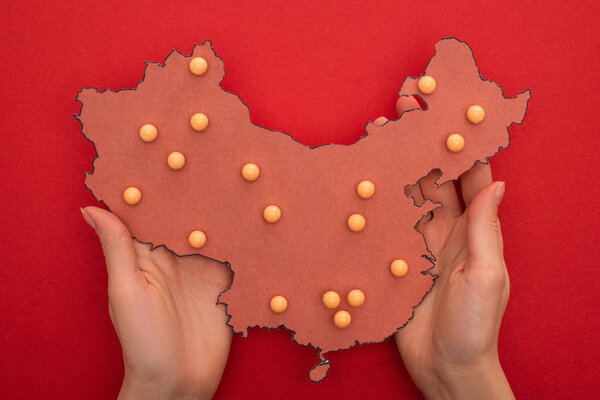 Top view of woman holding layout of china map with push pins on red background 