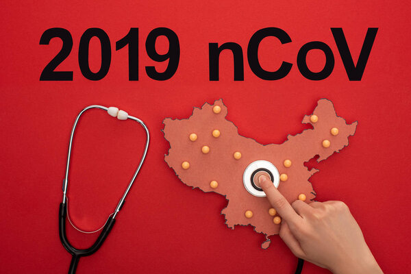 Top view of woman putting stethoscope on layout of china map with 2019 ncov lettering on red background