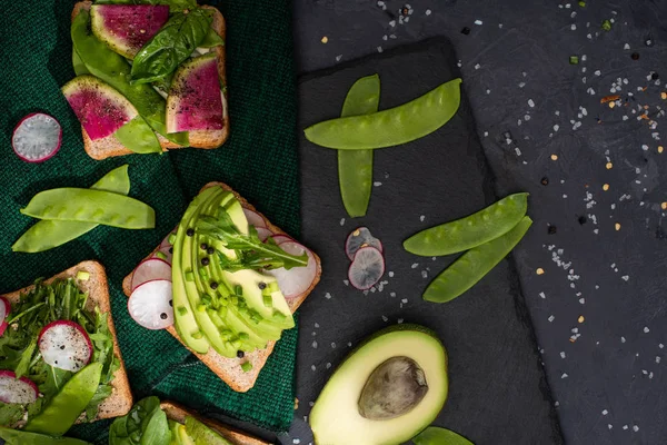 top view of vegetarian toasts with fresh vegetables on cloth and stone board