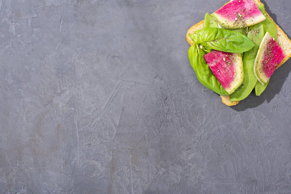 top view of toast with green peas, basil and radish on stone table