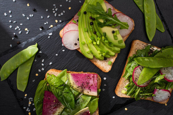 top view of fresh toasts with vegetables on stone board with pepper and salt