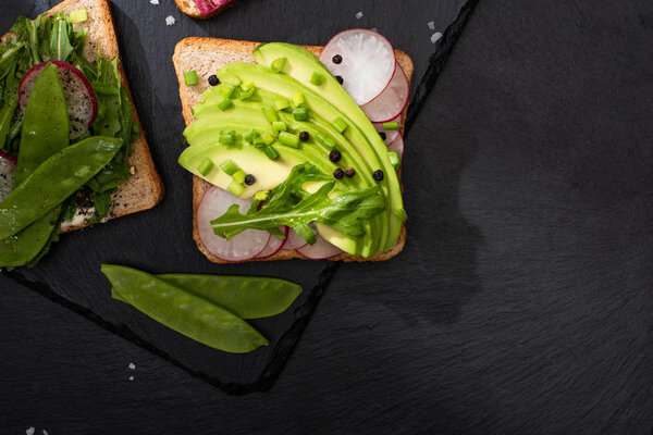 top view of fresh sandwiches with radish and avocado on stone board with pepper and salt