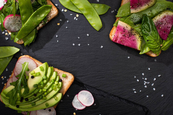 top view of vegetarian toasts with vegetables on stone board with pepper and salt