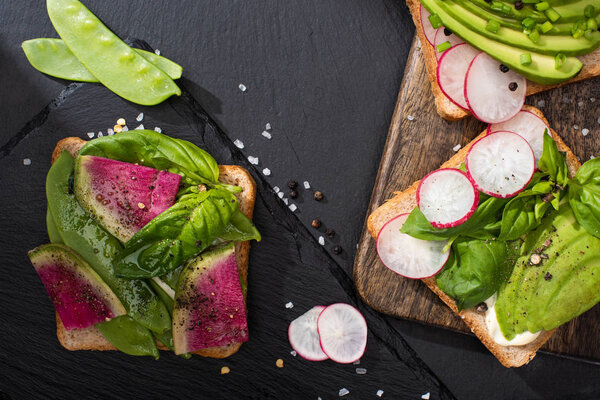 top view of healthy toasts with vegetables on stone and wooden boards with pepper and salt