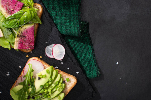 top view of vegetarian healthy sandwiches with radish and avocado on cloth and stone board