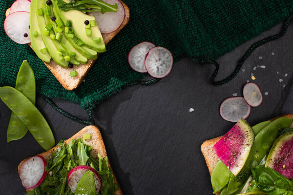 top view of fresh sandwiches with radish, greens and avocado on cloth
