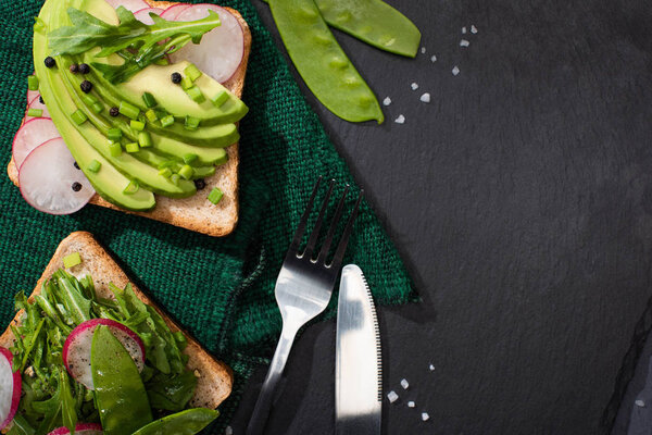 top view of vegetarian organic toasts with fresh vegetables on cloth with fork and knife