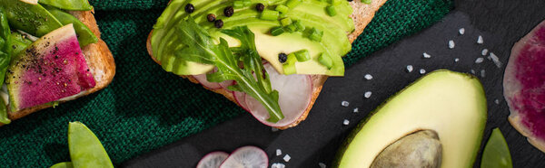 panoramic shot of fresh toasts with radish and avocado on green cloth