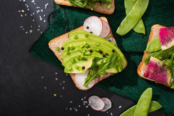 top view of fresh toasts with radish and avocado on green cloth