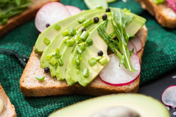 close up of fresh toasts with radish, green onion and avocado on cloth