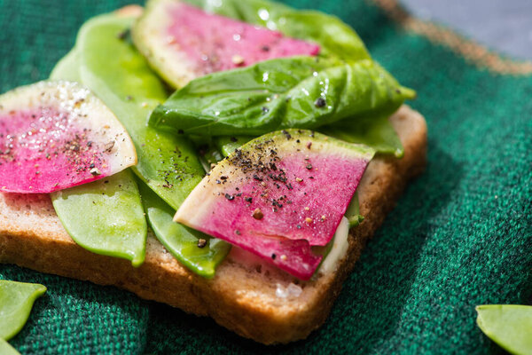 close up of toast with radish, green peas and basil on cloth