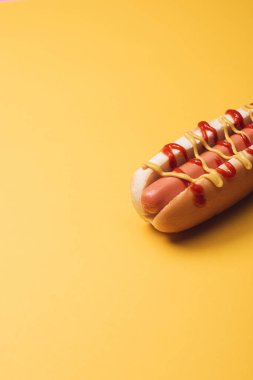 one yummy hot dog with sausage, mustard and ketchup on yellow  clipart