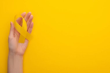 Partial view of female hand with yellow ribbon on colorful background, international childhood cancer day concept  clipart