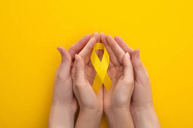 Cropped view of male and female hands with yellow ribbon on colorful background, international childhood cancer day concept clipart