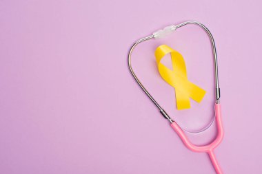 Mor arka planda sarı kurdele ve pembe steteskop, uluslararası çocukluk kanseri günü konsepti