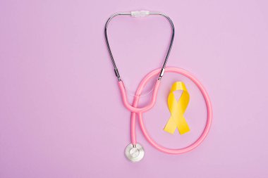 Mor arka planda pembe steteskoplu sarı kurdele, uluslararası çocukluk kanseri günü konsepti
