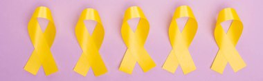 Flat lay with yellow awareness ribbons on violet background, panoramic shot, international childhood cancer day concept clipart
