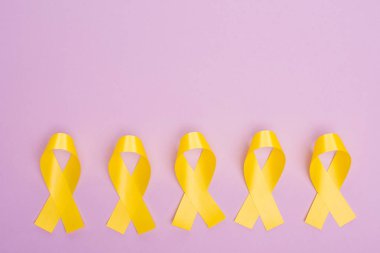 Flat lay with yellow awareness ribbons on violet, international childhood cancer day concept clipart