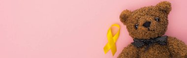 Top view of yellow ribbon and teddy bear on pink background, panoramic shot, international childhood cancer day concept clipart