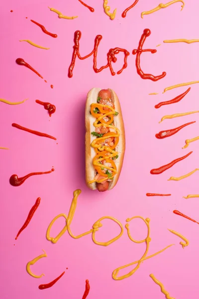 stock image top view of unhealthy hot dog on pink with word hot dog written with ketchup and mustard