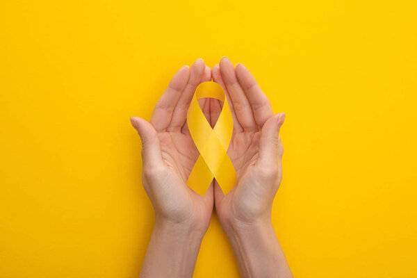 Partial view of female hands with yellow awareness ribbon on colorful background, international childhood cancer day concept