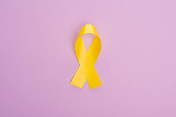 Top view of yellow ribbon on violet background, international childhood cancer day concept