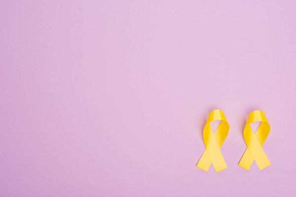 Flat lay with yellow awareness ribbons on violet background, international childhood cancer day concept