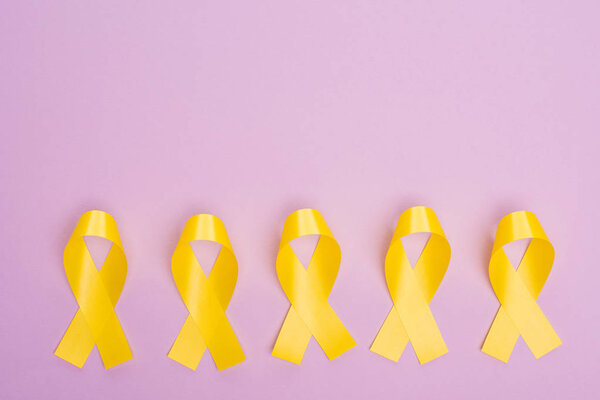 Flat lay with yellow awareness ribbons on violet, international childhood cancer day concept