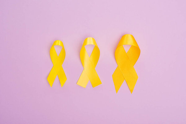 Top view of yellow awareness ribbons on violet background, international childhood cancer day concept